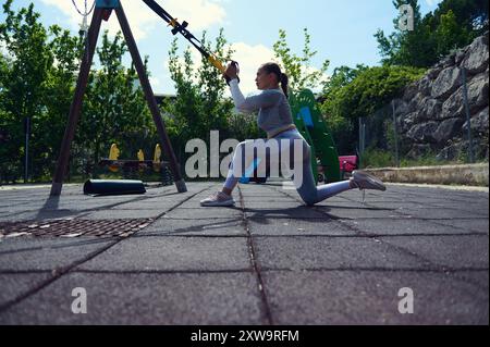 Die FIT Woman führt in einem Fitnessstudio im Freien TRX-Federungsübungen durch. Sie konzentriert sich auf Kraft, Gleichgewicht und Fitness und genießt sonniges Wetter und Open Air. Stockfoto