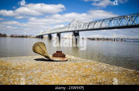 Ankerbolzen auf rostgebeiztem Betonblock mit Wasser und Brücke im Hintergrund Stockfoto