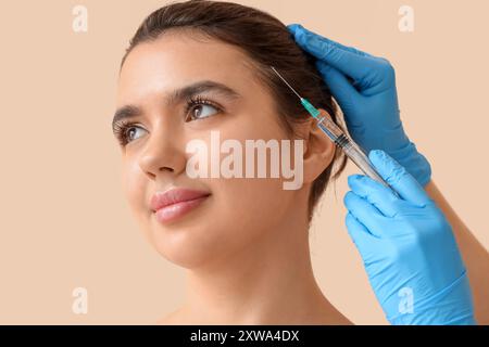 Junge Frau bekommt Haarspritze auf beigefarbenem Hintergrund, Nahaufnahme Stockfoto