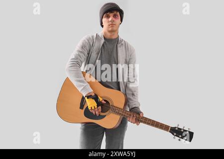 Junger Obdachloser, der Gitarre auf hellem Hintergrund spielt Stockfoto