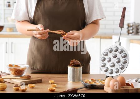 Frau kocht leckere, walnussförmige Kekse mit gekochter Kondensmilch am Holztisch in der Küche Stockfoto