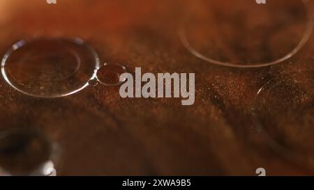 Serumblasen. Ölflüssigkeit. Defokussierte Bronze goldene Farbe transparent schimmernde Glitzer Textur Farbe Wasser runde Tropfen schwimmende abstrakte Kunst Hintergrund. Stockfoto