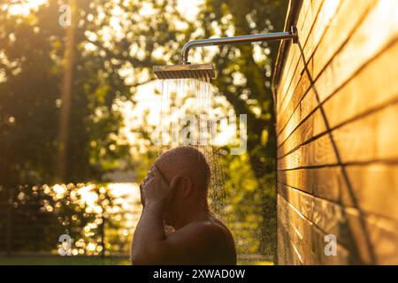 Mann unter Sonnenuntergang Dusche im Freien. Konzept der Entspannung und erfrischendes Wassererlebnis Stockfoto