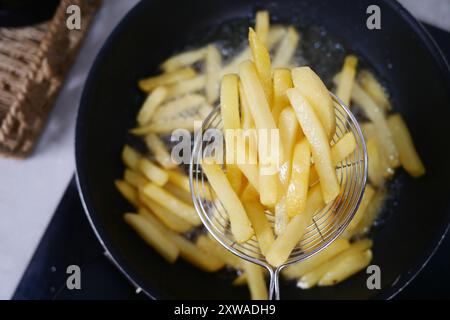 Golden French Fries werden fachmännisch in einer heißen Pfanne mit Öl frittiert Stockfoto