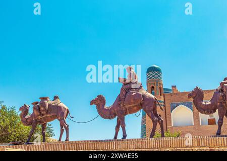 Skulpturengruppe einer Karawane mit Kamelen, die Güter entlang der Seidenstraße in der Nähe der alten Stadtmauern transportieren. Chiwa, Usbekistan - 17. Juli 2024. Stockfoto