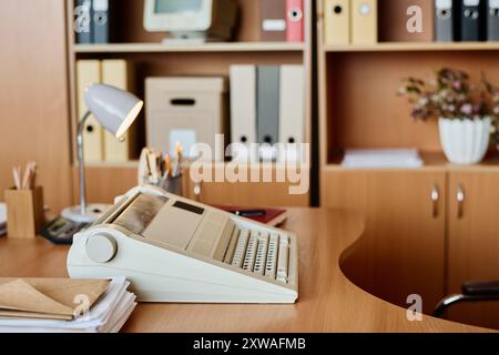 Klassische Büroumgebung mit Vintage-Schreibmaschine auf Holztisch, Regalen mit Aktenmappen und verschiedenen Büromaterialien schaffen nostalgische Atmosphäre Stockfoto