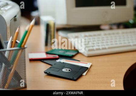 Nahaufnahme eines hölzernen Schreibtisches mit Vintage-Disketten, verschiedenen Bleistiften in einem Halter und Computertastatur im Hintergrund, die an Nostalgie erinnert Stockfoto