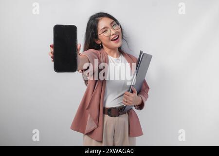 Schöne asiatische Geschäftsfrau in Brille, die ein Dokument hält, das einen Kopierraum auf ihrem Telefonbildschirm darstellt, isoliert durch weißen Hintergrund. Stockfoto