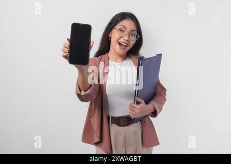 Schöne asiatische Geschäftsfrau in Brille, die ein Dokument hält, das einen Kopierraum auf ihrem Telefonbildschirm darstellt, isoliert durch weißen Hintergrund. Stockfoto