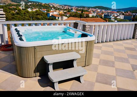 Whirlpool im Freien auf der sonnigen Dachterrasse mit sprudelndem Wasser und komfortablen Sitzgelegenheiten mit wunderschönem Blick auf die touristische Stadtlandschaft. Ort zum Entspannen und Stockfoto