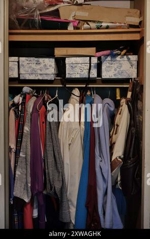 Eine Garderobe voll alter Klamotten auf Kleiderbügeln, Schuhkartons mit Fotos, Pappe und Geschenkpapier, ältere Eltern, die in ihrem eigenen Zuhause leben, Stockfoto