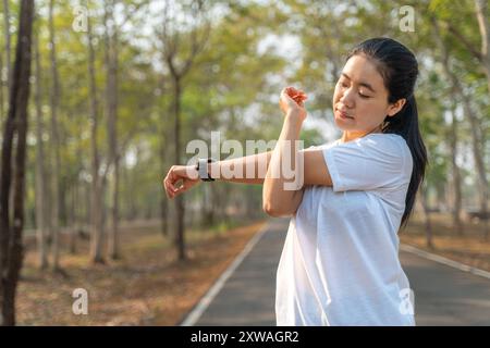 Junge Läuferin, die ihre Arme und Beine ausdehnt, bevor sie ihren morgendlichen Lauf in einem örtlichen Laufpark beginnt Stockfoto