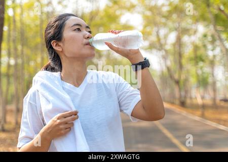 Junge Frau, die Wasser aus einer Plastikflasche trinkt, nachdem sie morgens in einem örtlichen Laufpark gelaufen ist Stockfoto