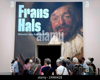 Frans Hals - Ausstellung Berlin DEU, Deutschland, Berlin, 16.07.2024 Besucher vor dem Eingang mit dem Plakat Bild der froehlich Trinker von 1628-1630 in der Ausstellung Frans Hals Meister des Augenblicks in der Gemaeldegalerie am Kulturforum in Berlin Deutschland. Die Sonderausstellung laeuft vom 12.07.2024 bis 03.11.2024. Der Portraetmaler Frans Hals zaehlt neben Rembrandt und Vermeer zu den herausragenden niederlaendischen Malern des 17. Jahrhundert. Neben ausdrucksstarken Bildnissen der Haarlemer Elite malte er als erster Küstler Hollands auch soziale Außenseiter als Individue Stockfoto