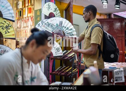 (240819) -- WUHAN, 19. August 2024 (Xinhua) -- Lugazo Abubakar Lugazo (hinten) schaut einen Ventilator in einem Geschäft in Wuhan, Zentralchinas Provinz Hubei, 24. Juni 2024 an. Lugazo Abubakar Lugazo, ein 30-jähriger Tansania, promoviert derzeit an der Central China Normal University (CCNU) in Wuhan. Neben seinem Studium ist er auch Leiter eines Freiwilligen-Service-Teams, das sich aus internationalen Studenten zusammensetzt. Lugazos Zuneigung für China begann während seines Bachelorstudiums in Tansania. Angeregt von einem chinesischen Lehrer an einem Konfuzius-Institut, begann Lugazo seine Reise, Chinesisch A zu lernen Stockfoto