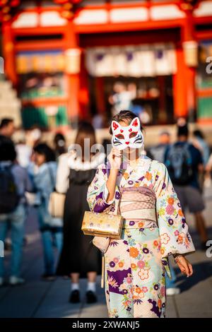 Eine Frau in einem Kimono mit einer Maske im Gesicht und einer Handtasche an der Hand. Kyoto, Japan. Stockfoto