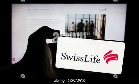 Person mit Smartphone mit Logo der Versicherungsgesellschaft Swiss Life Holding AG vor der Website. Schwerpunkt auf dem Display des Telefons. Stockfoto