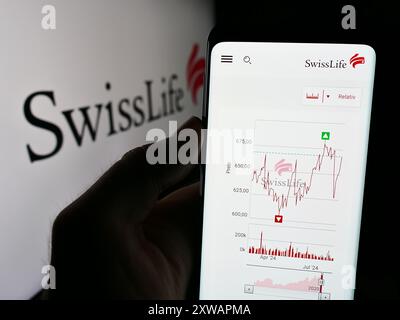 Person mit Smartphone und Website der Versicherungsgesellschaft Swiss Life Holding AG vor dem Firmenlogo. Konzentrieren Sie sich auf die Mitte des Telefondisplays. Stockfoto