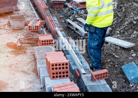 Hart arbeitender Maurer, der Betonblöcke auf Betongrundlagen auf einer neuen Wohnsiedlung legt. Bekämpft die Wohnungskrise, indem ihr mehr Geld aufbaut Stockfoto