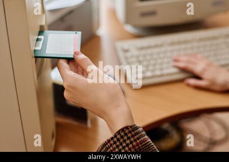 Nahaufnahme von zwei Händen im Büro, einer, der Diskette in das Laufwerk einlegt, der andere auf der Tastatur, zeigt klassische Computertechnologie und Hände bei der Arbeit Stockfoto