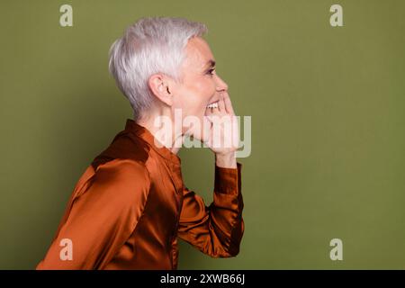 Foto-Porträt der hübschen pensionierten weiblichen Schrei Profil Leere Raum tragen trendige braune Formalwear isoliert auf khakifarbenem Hintergrund Stockfoto
