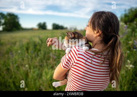 Frau hält gefleckte Katze auf der Schulter, geht mit Haustier in der Natur. Haustierbesitzer, Haustiersitzer auf dem Land Stockfoto