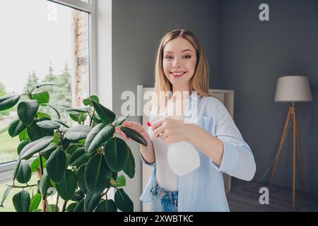 Foto von entzückender süßer junger Dame tragen blaues Hemd, die Pflege Pflanze im Innenraum Haus umschlägt Stockfoto