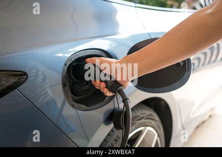 Mann, der sein Elektroauto auflädt. Nahaufnahme des Einsteckens des elektrischen Steckverbinders am Fahrzeug. Stockfoto