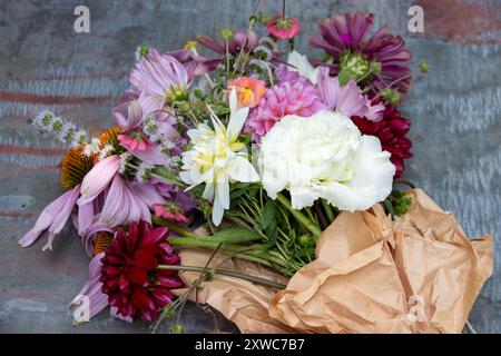 Bunter Blumenstrauß in braunem Papier auf rustikaler Oberfläche Stockfoto