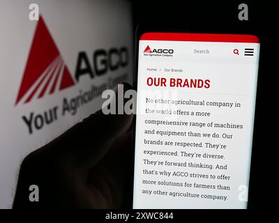 Person, die ein Mobiltelefon hält, mit der Website des US-amerikanischen Landmaschinenunternehmens AGCO Corporation vor dem Logo. Konzentrieren Sie sich auf die Mitte des Telefondisplays. Stockfoto