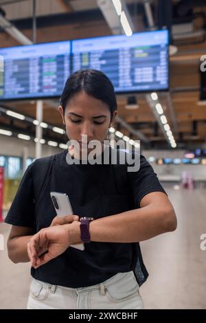 Junge Frau, die Telefon und Smart Watch überprüft und auf verspäteten Flug wartet Stockfoto