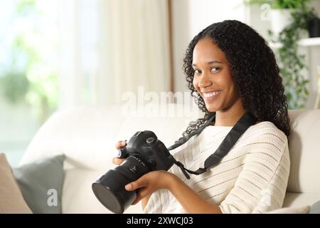 Ein glücklicher schwarzer Amateurfotograf, der zu Hause auf einer Couch sitzt, sieht dich an Stockfoto