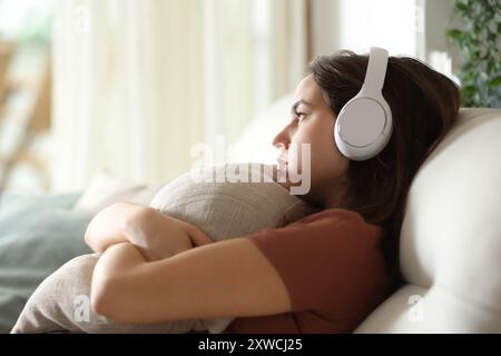 Traurige und melancholische Frau, die zu Hause Musik mit Kopfhörern hört Stockfoto