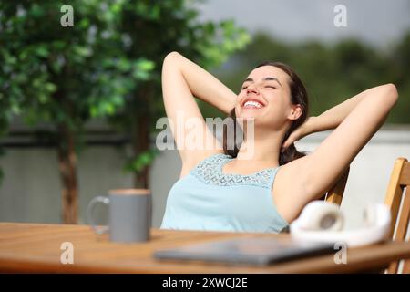 Glückliche Frau, die in einem Garten sitzt und sich entspannt und sonnt Stockfoto