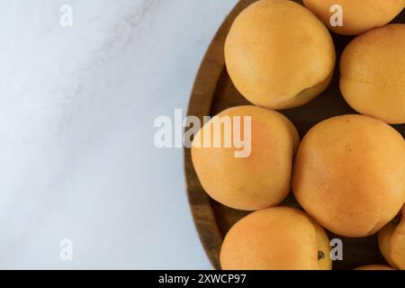 Reife Aprikosen auf einem Holzteller, Blick von oben. Frische natürliche Aprikosen, köstliches Sommerdessert, auf Marmorarbeitsfläche, Nahaufnahme, hohe Auflösung. Stockfoto