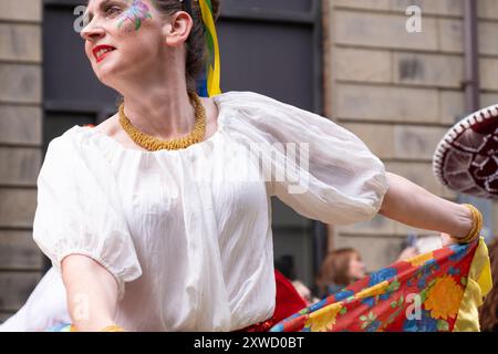 Frau in farbenfrohem Kleid mit gemalter Dekoration auf Gesichts tanzen bei der jährlichen Karnevalsparade in Belfast Mela im Stadtzentrum. Belfast, Großbritannien - 17. August 2024. Stockfoto