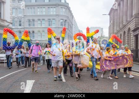 Menschen, die an der jährlichen Belfast Mela Carnival Parade teilnehmen, bedeckt mit Farbenkraft Gulal, Danske Buchstaben in Regenbogenballons. Belfast, Großbritannien - August 2024. Stockfoto