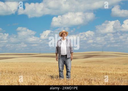 Ein reifer Bauer trägt einen Strohhut und steht auf einem Weizenfeld Stockfoto