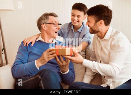 Sohn Und Enkel Gratulieren Opa Und Geben Geschenk Sitzend Zu Hause Stockfoto