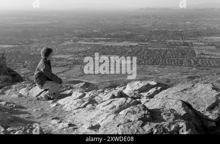 Eine Weiße im Alter von 50-60 Jahren sitzt auf einem Felsen am Dobbins Lookout, South Mountain Park, Phoenix, Arizona, USA. Stockfoto