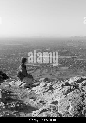 Eine Weiße im Alter von 50-60 Jahren sitzt auf einem Felsen am Dobbins Lookout, South Mountain Park, Phoenix, Arizona, USA. Stockfoto