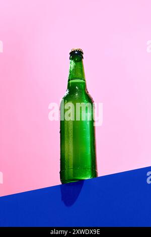 Grüne Glasflasche auf blaurosa Hintergrund. Modell. Bier, Limonade, Limonade. Einfache und stilvolle Basis für das Produktbranding Stockfoto