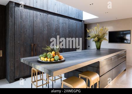 Gelber Besen (Cytisus scoparius) und Obst auf der Küchenarbeitsfläche mit rauen, behauenen Cupbaorden in luxuriösem, modernem britischen Haus. London, Großbritannien Stockfoto