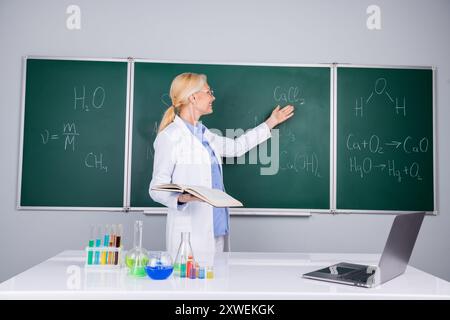 Foto von intelligenter, intelligenter Schullehrerin trägt weißen Gewand und erklärt Lektion isoliert auf grünem Bretthintergrund Stockfoto