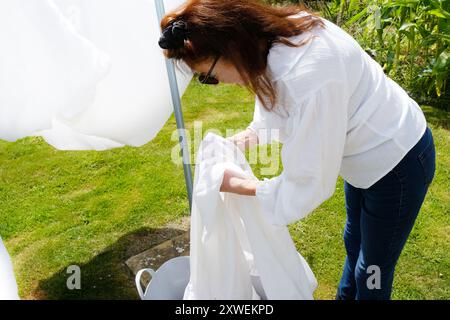 Reife Frau, die weiße Bettlaken an einer rotierenden Wäscheleine hängt - John Gollop Stockfoto