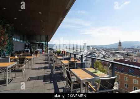 Linz, Österreich. August 2024. Tische eines Restaurants auf einer Terrasse auf dem Schlosshügel mit Panoramablick auf die Stadt Stockfoto