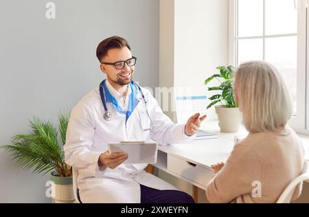Ältere ältere grauhaarige Patientin sitzt während der Untersuchung am Schreibtisch in der Arztpraxis. Stockfoto