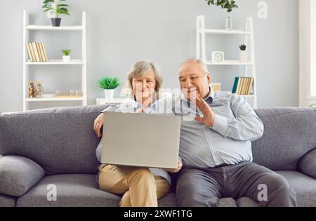 Glückliches pensioniertes Paar, das mit der Hand winkt und mit der Webcam Videoanrufe auf dem Laptop zu Hause macht. Stockfoto