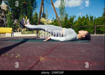 Eine Frau führt in einem Park Suspensionstraining durch und betont ihr Engagement für Fitness- und Outdoor-Workouts, wobei der Schwerpunkt auf Kernkraft und -Stärke liegt Stockfoto