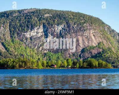 Einzelnes rotes Haus auf der Insel Oeyni im See Bygdlandsfjord, steiler Berg, Setesdal Valley, Norwegen Stockfoto